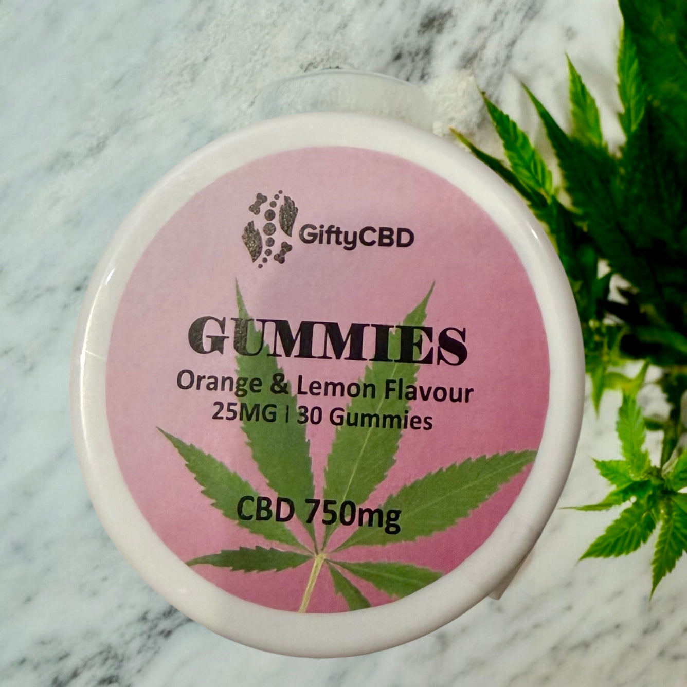 Container of GiftyCBD gummies with a pink label on a marble surface with cannabis leaves.